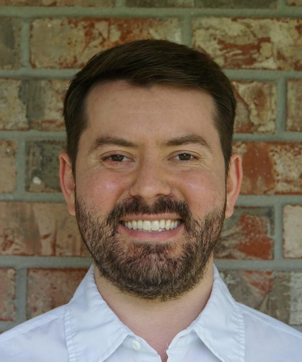 Chris Weber, smiling, in a white shirt against a brick wall
